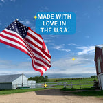 American flag waving with farm buildings and blue sky.