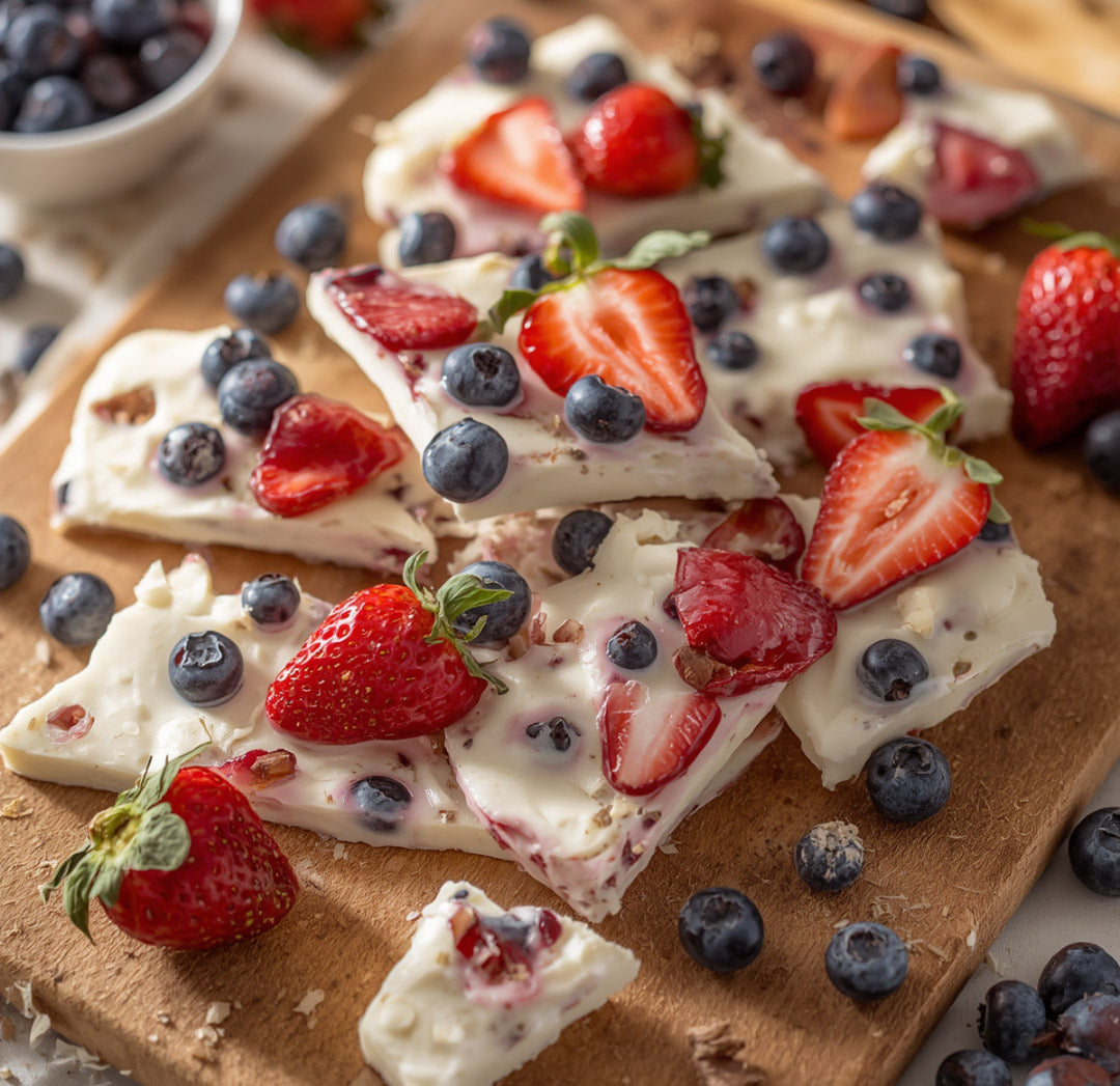 Red, white and blue collagen yogurt bark broken into pieces on a wood board with fresh strawberries and blueberries